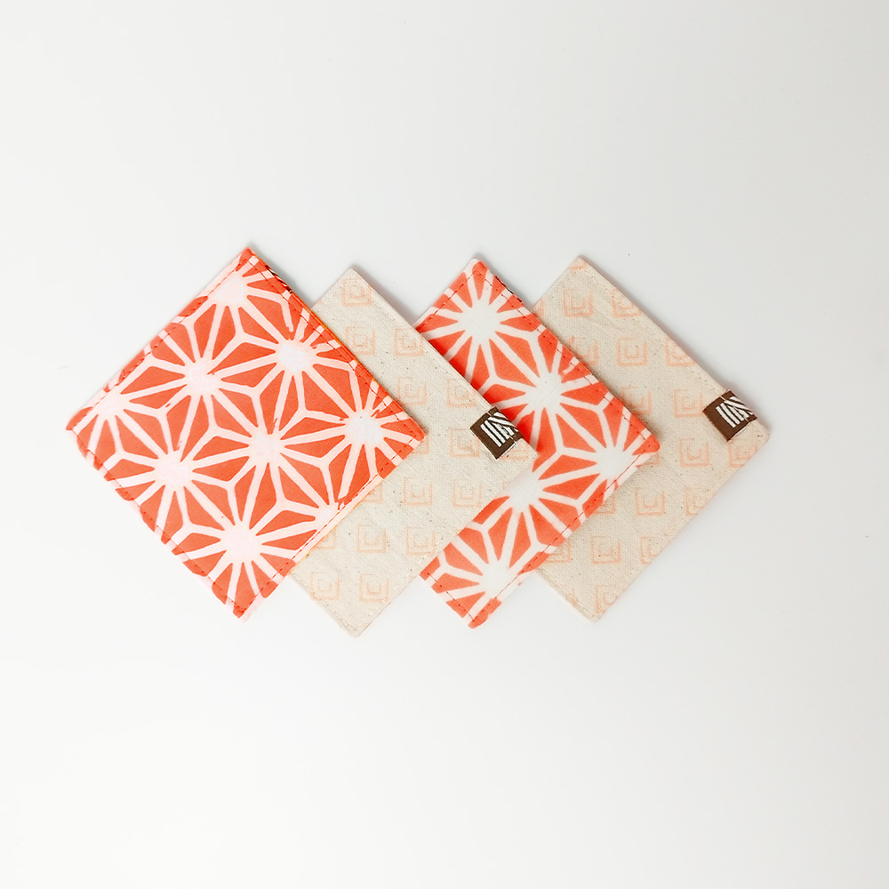 Artisan-crafted peach batik coasters with starburst pattern, set of four coasters, Square cotton coasters featuring peach firework batik design, reversible sides in matching tones, handcrafted by Malaysian artisans. Peach and white batik coasters in starburst motif, reversible fabric with Batik Boutique logo box, ideal for home décor or gifting. Perfect for  drinking, parties, Events
Stocking stuffer. Fabric coasters. Batik Boutique