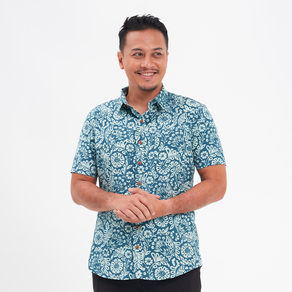 a man wearing a batik shirt in the pattern teal ukir against a white background