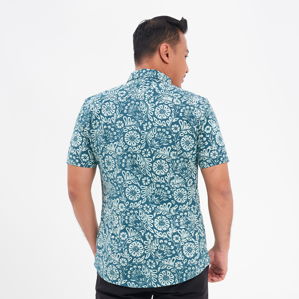 a man showcasing the details on the back of a batik shirt against a white background