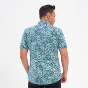a man showcasing the details on the back of a batik shirt against a white background