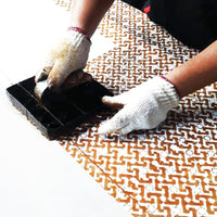 An artisan is batik blocking arabesque pattern on white fabric