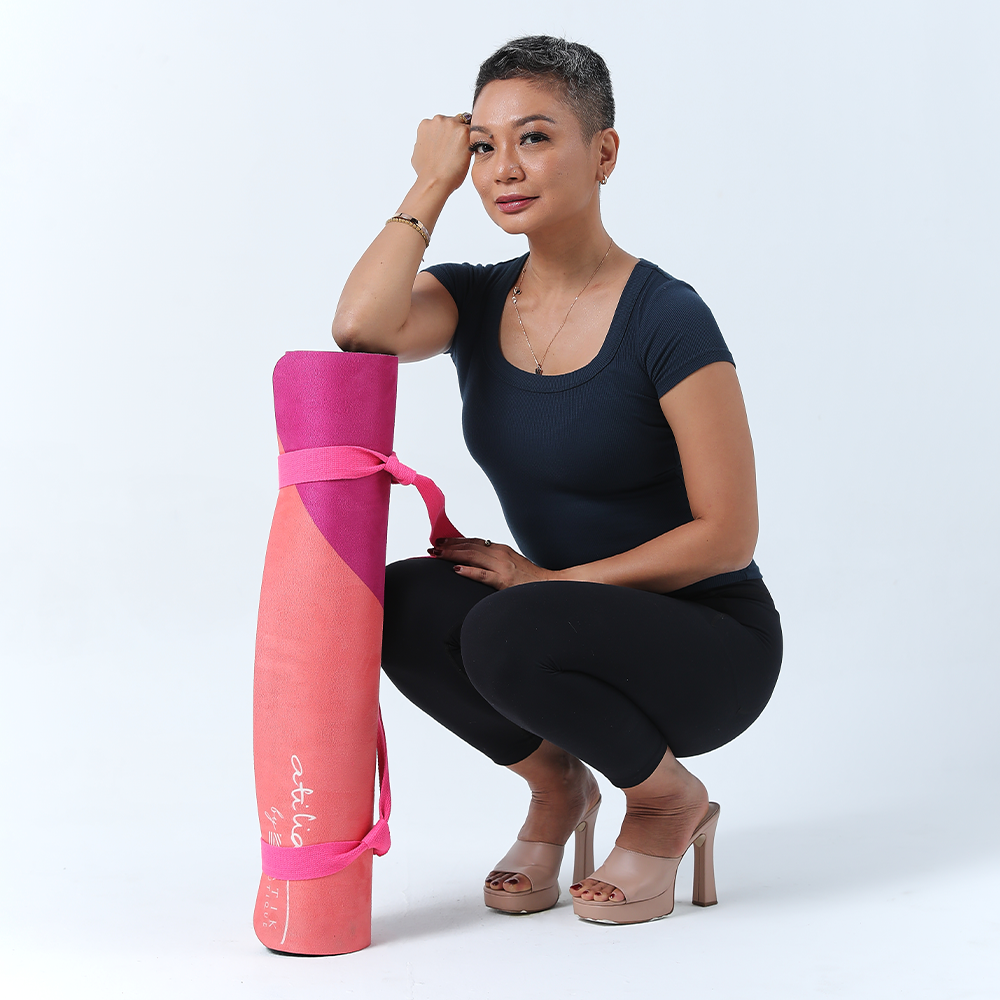 atilia haron posing in front of a white background with her yoga mat fuchsia cat yogis