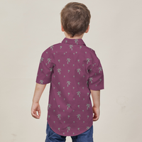 a boy posing with his back to the camera in front of a neutral background while wearing a batik shirt in the pattern fuchsia palm