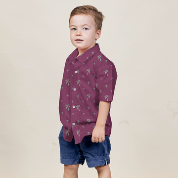 a boy posing in front of a neutral background while wearing a batik shirt in the pattern fuchsia palm