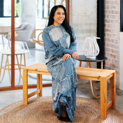 Woman seated on a wooden bench wearing a slate blue batik caftan pareo