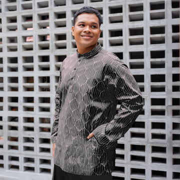 a male model posing in a batik kurta in the pattern jet bawang against a concrete wall