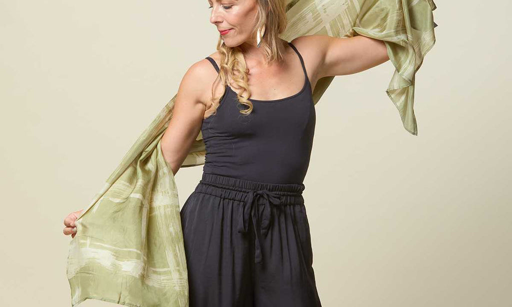 Woman playing around with long batik scarf in olive cotton silk.