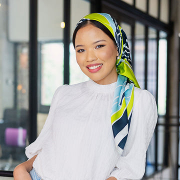 A hijabi woman is wearing batik scarf in batik print call teal rimba leaning at rail