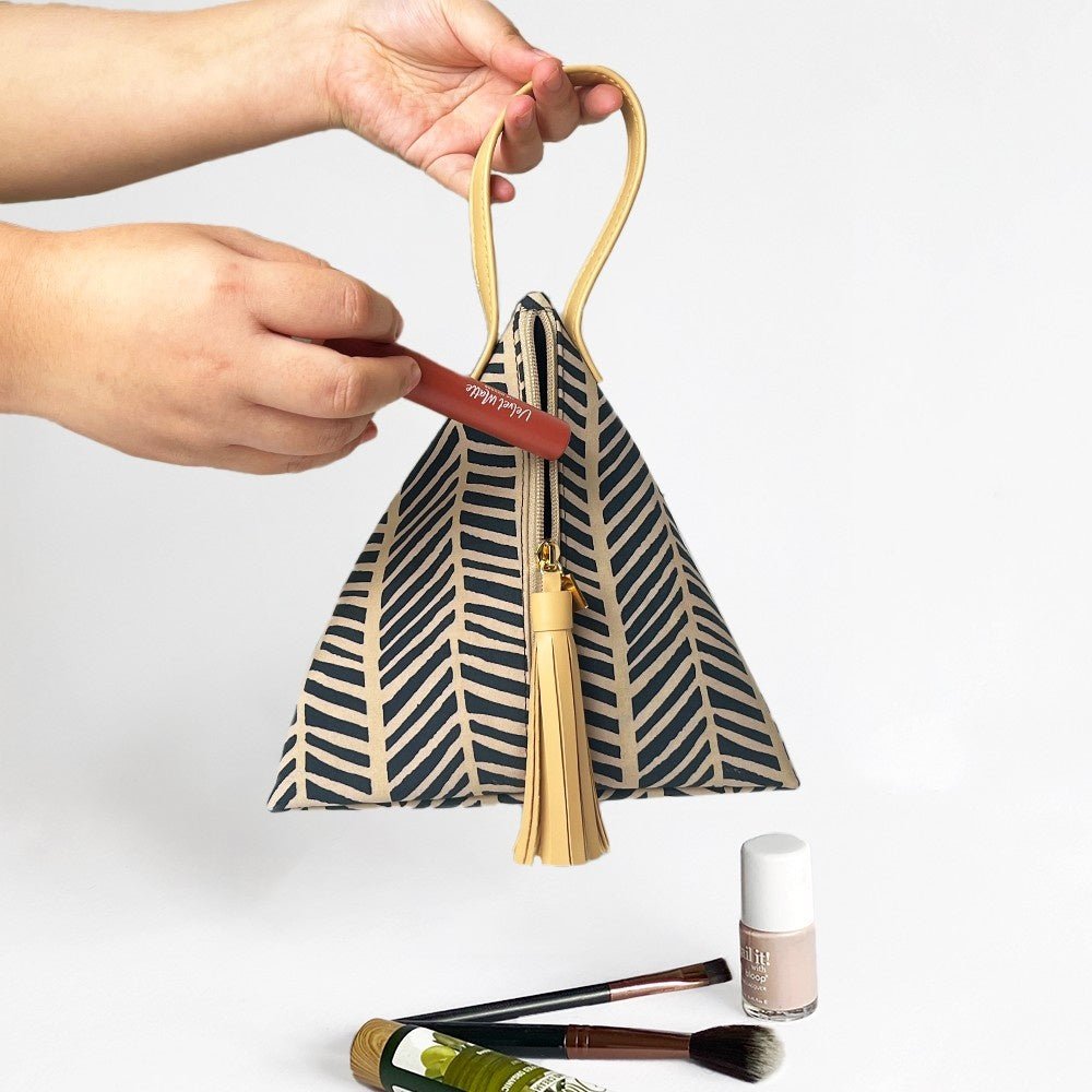 Hand placing makeup into Batik Boutique’s Black Banana Leaf Ketupat Bag, perfect for cosmetics or small essentials.