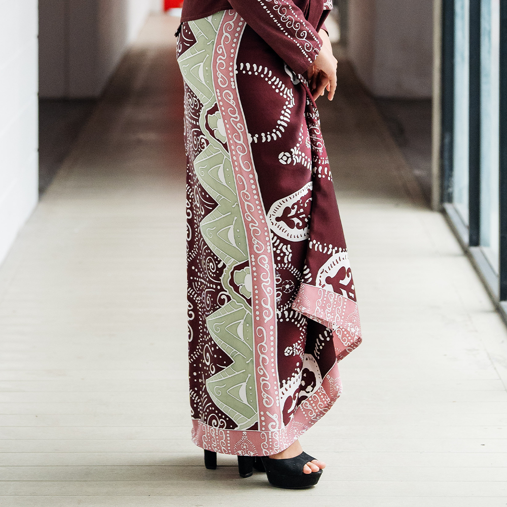 Elegant Batik Pareo in Maroon Petola – A model wearing a maroon batik pareo with intricate motifs, styled with matching outerwear