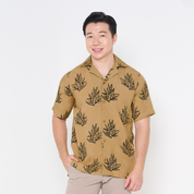 a male model posing in front of a white background in a batik shirt in cuban cutting in the pattern tan olive leaf