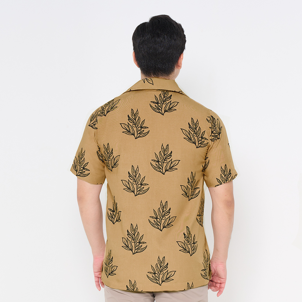 a man posing against a white background with his back to the camera to showcase the details on the back of the batik shirt in the pattern tan olive leaf