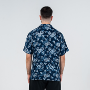 Back view of a man wearing the Men’s Cuban Shirt in Navy Blossom, a batik design featuring hand-painted floral motifs in shades of blue and white.