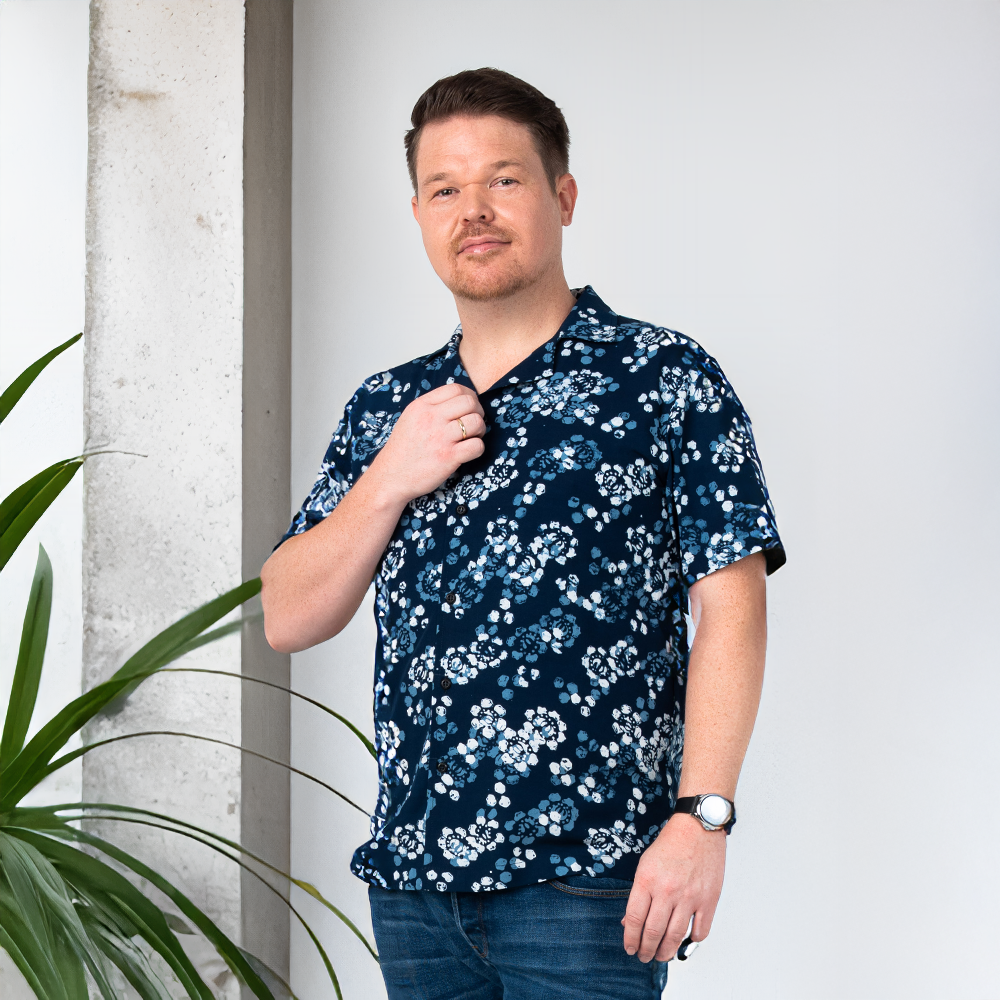Lifestyle photo of a man wearing the Men’s Cuban Shirt in Navy Blossom, styled casually in a modern setting to highlight its unisex floral batik design.