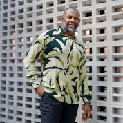 Man wearing Forest Palma batik shirt styled for casual or workwear, standing against a textured wall.