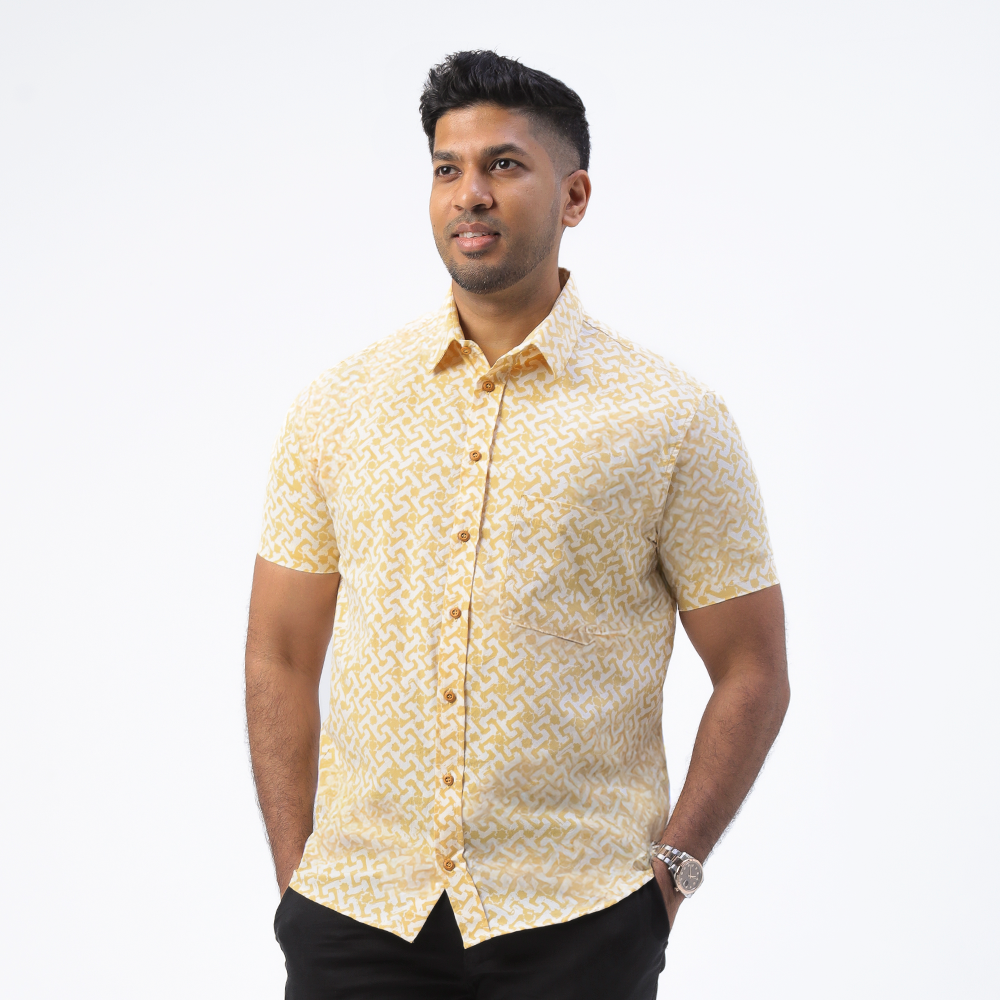 a man posing in a batik shirt in the pattern mustard arabesque against a white background