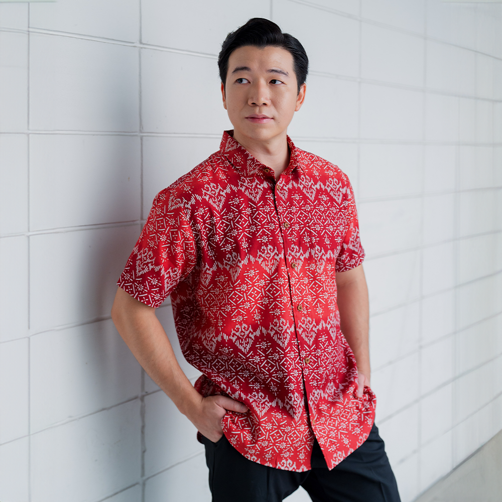 a male model posing against a white background in a lifestyle photo in the batik shirt called red anyam