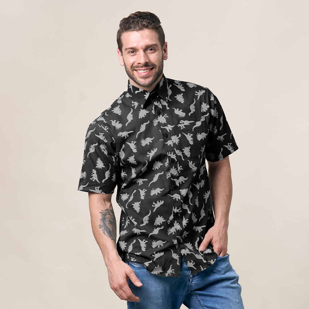 a man wearing a batik shirt in the pattern grey dinosaurs, posing in front of a neutral background