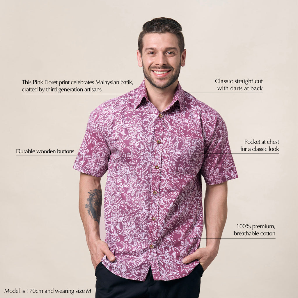 A man striking a confident pose against a neutral background, showcasing the authenticity of his batik shirt in the elegant Pink Floret pattern
