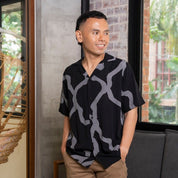 Man wearing a  Cuban jet chain patterned shirt standing indoors with a neutral background