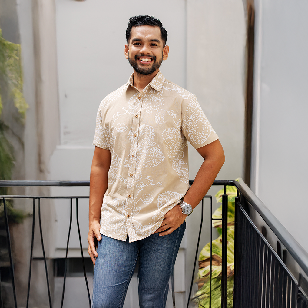 Man wearing a beige patterned tan orchid shirt and blue jeans standing on a balcony.