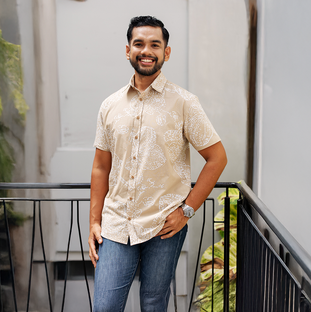 Man wearing a beige patterned tan orchid shirt and blue jeans standing on a balcony.