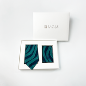 a white box photo of a teal snakeskin neck tie and pocket square against a white background with whit box