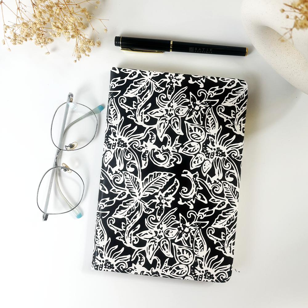 Black and white batik notebook with floral motif styled beside glasses and pen on white desk — Batik Boutique handmade stationery.