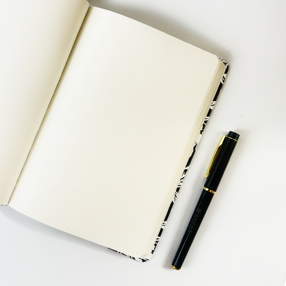Open batik notebook with cream blank pages and Batik Boutique pen placed on white background.