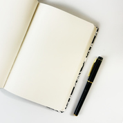 Open batik notebook with cream blank pages and Batik Boutique pen placed on white background.