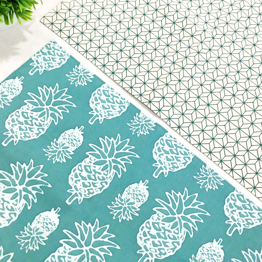 a photo showcasing two reversible batik placemats in the print turquoise pineapple