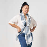 A woman is standing in front of white wall, wearing grey brush color batik long scarf, handcrafted and artisan made locally in Malaysia