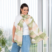 Woman wearing Batik Boutique’s Moss Bukit batik scarf in soft green and peach tones, styled casually with white top and jeans