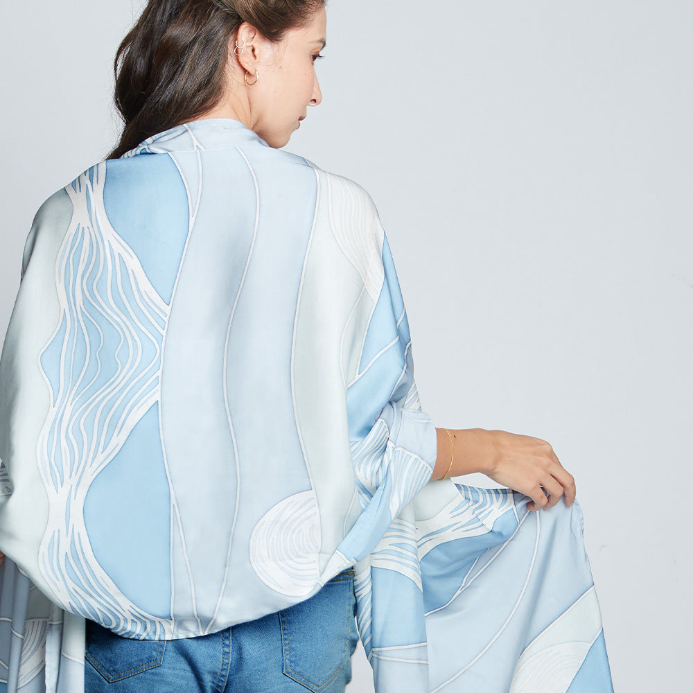 Full view of a woman wearing a white shirt and blue batik cotton silk scarf in print that was hand-painted by artisans of Batik Boutique. 