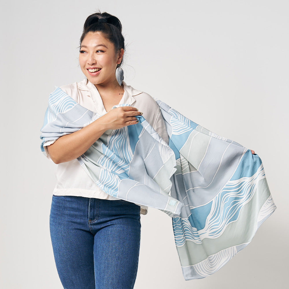 A woman is standing in front of white wall, wearing blue color batik long scarf, handcrafted and artisan made locally in Malaysia