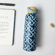 Blue patterned water bottle with wooden cap on a white surface next to a notebook and pen.