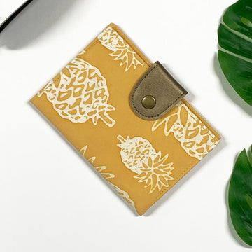 a lifestyle photo of a  passport cover made of batik in the pattern golden pineapple 