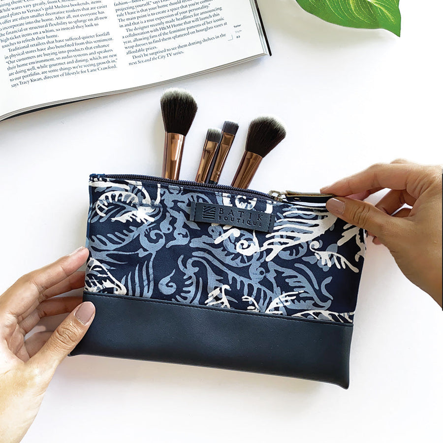 a lifestyle photo showcasing a zip pouch made of batik in the pattern blue nautical fern with props in front of a neutral background