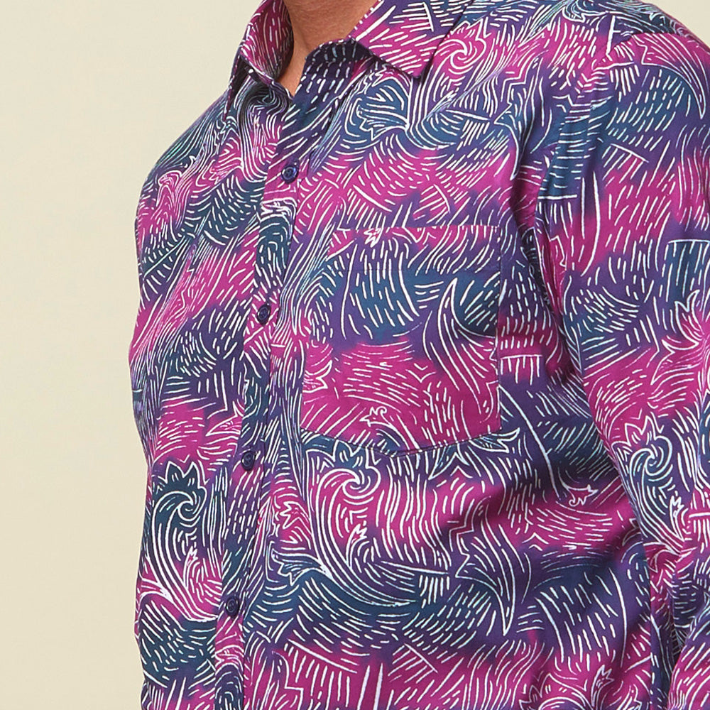 A closeup photo of man standing in front of beige background wearing maroon long sleeved shirt facing front