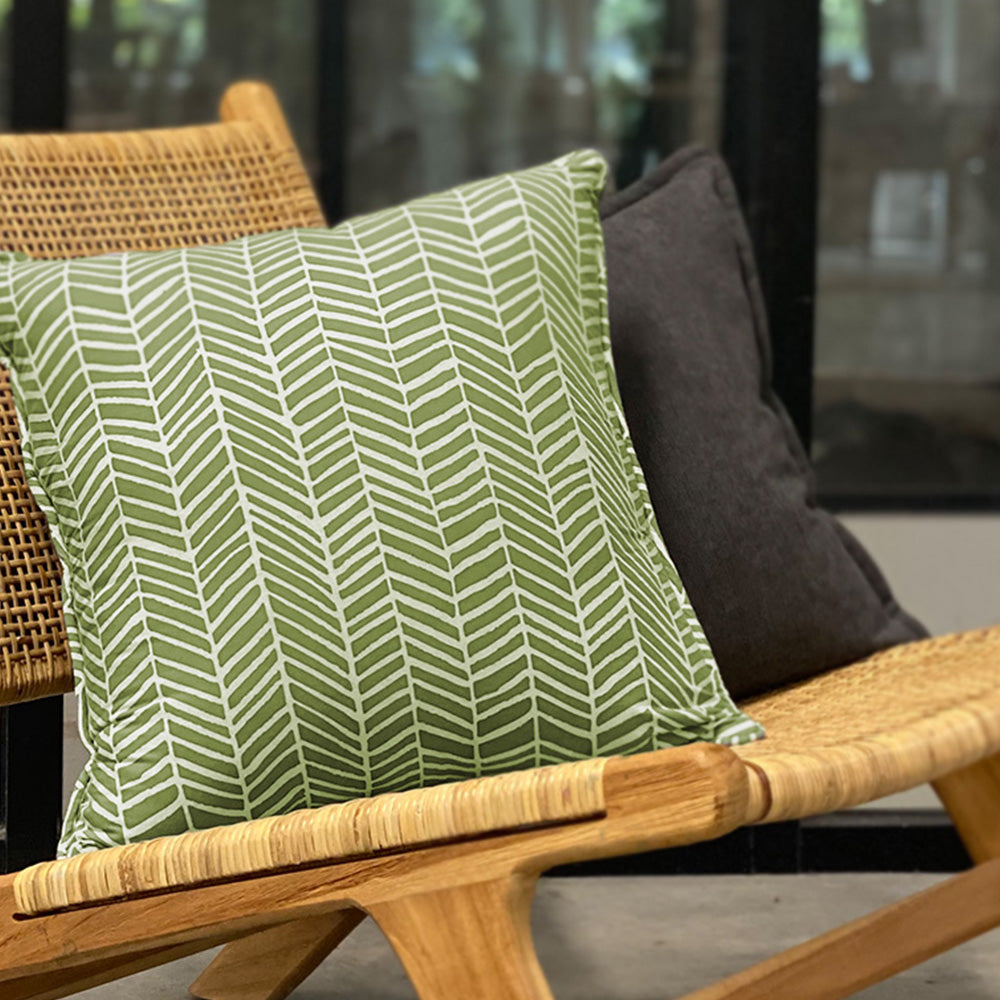 A lifestyle photo of batik pillow cover in sage banana leaf on a rattan chair