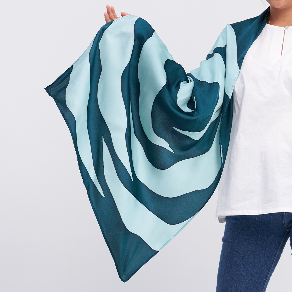 a woman model posing with a batik scarf in the pattern teal rose against a neutral background