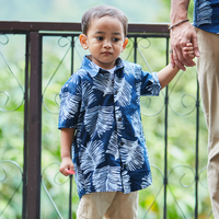 In a lifestyle photograph, a young boy, donned in a Navy Sawit patterned batik shirt, stands hand in hand with an adult