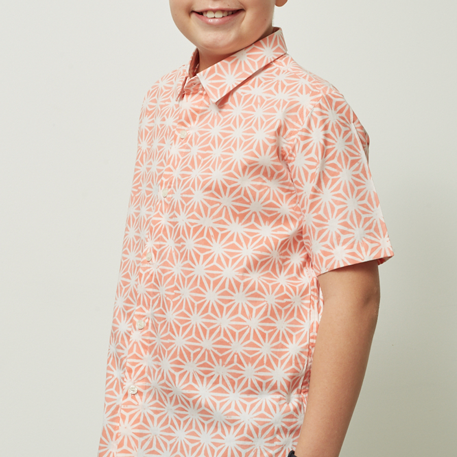 A captivating close-up photograph featuring a young boy wearing a Peach Firework patterned batik shirt against a neutral background