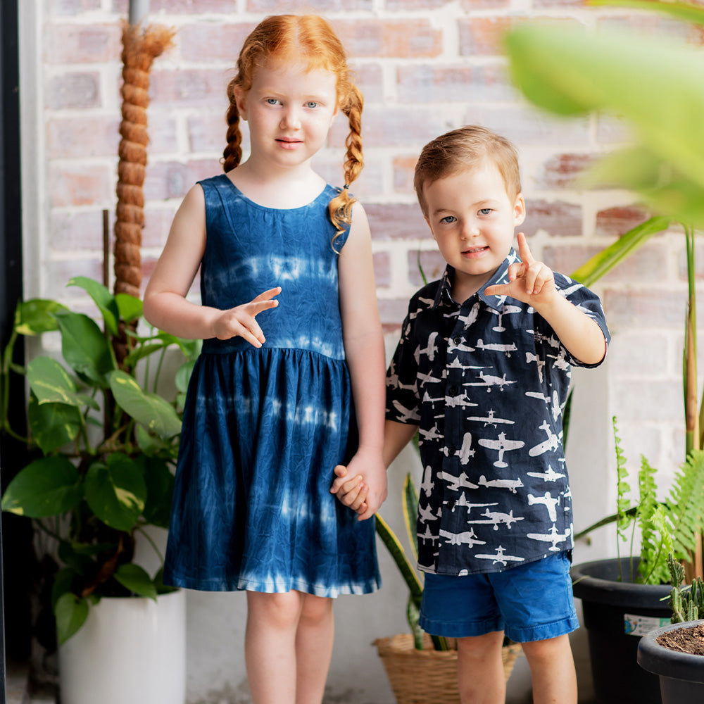 boy and girl standing in front of brick walls with greenery wearing batik dress and shirt in shibori navy wave and black airplane respectively