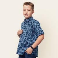 A youthful model elegantly posing against a neutral background, donned in a Midnight Arabesque patterned batik shirt