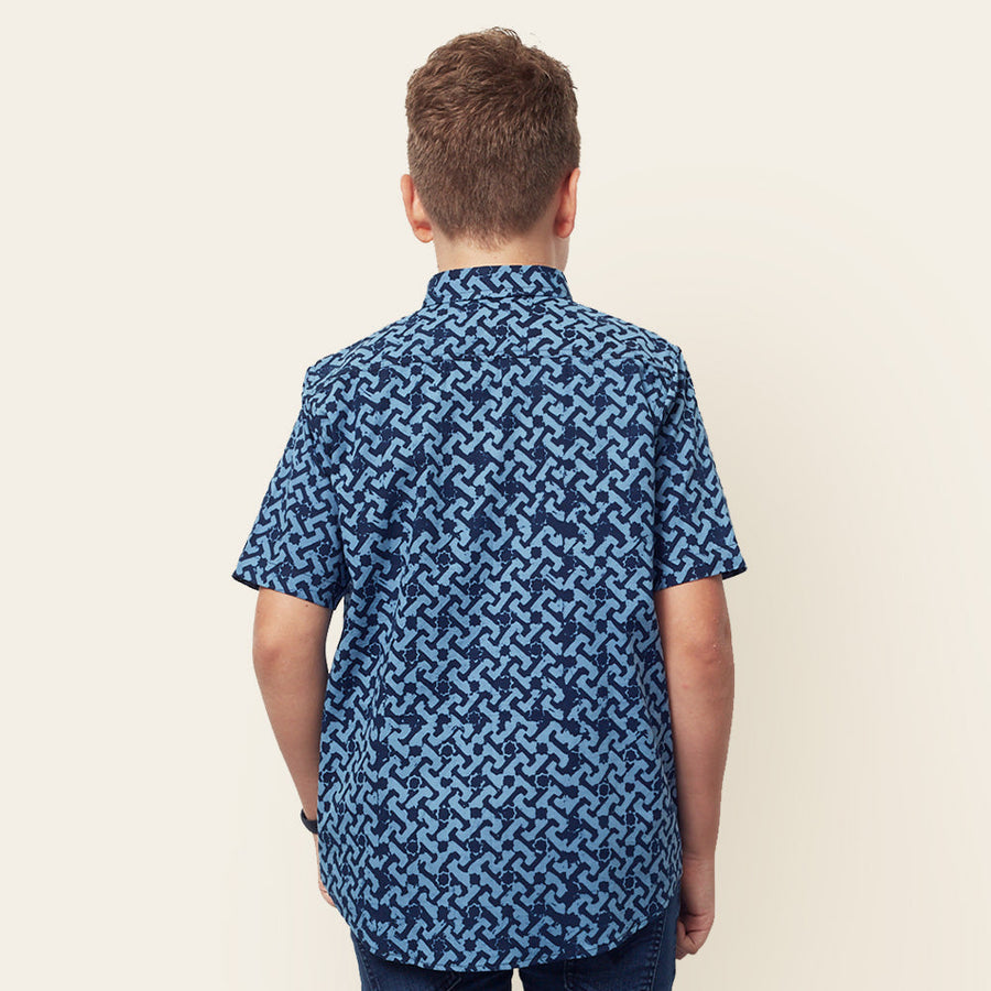 A boy confidently turning his back to the camera, showcasing the intricate details on the back of the Midnight Arabesque patterned batik shirt