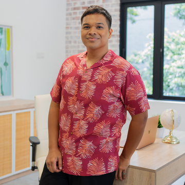 a male model leaning on a table while wearing an authentic batik shirt in the pattern crimson sawit in a lifestyle photo