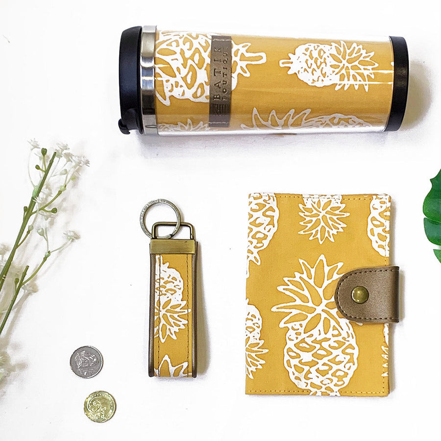 A lifestyle photo of yellow color batik in pineapple pattern. The photo included keyfob, passport cover and batik tumbler.