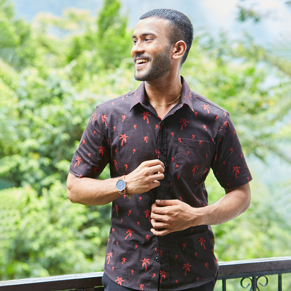 A man standing in the balcony wearing a black batik shirt with red palm motif