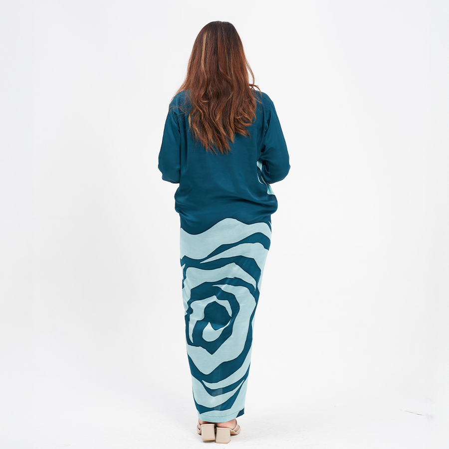 a female model facing away from the camera to show the details on the back of a batik caftan pareo in the pattern teal rose against a white background
